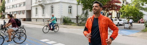 Mann joggt auf einer Straße mit blauem Radweg, im Hintergrund radeln Menschen.