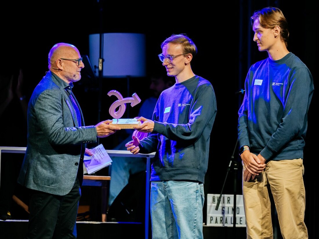 Verkehrsminister Hermann übergibt die Trophäe für die Kategorie Kommunikation an zwei junge Männer.