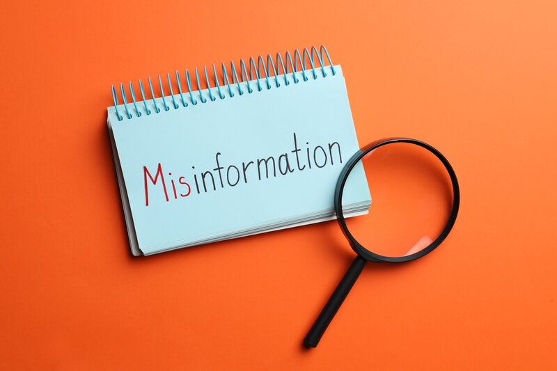 Blaues Notizbuch mit der handschriftlichen Aufschrift „Misinformation“ und eine Lupe auf leuchtend orangefarbenem Hintergrund.