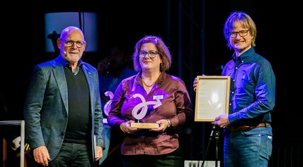 Verkehrsminister Hermann, eine Frau und ein Mann, zusammen auf der Bühne mit der Trophäe für die Kategorie Garantiert Mobil. 