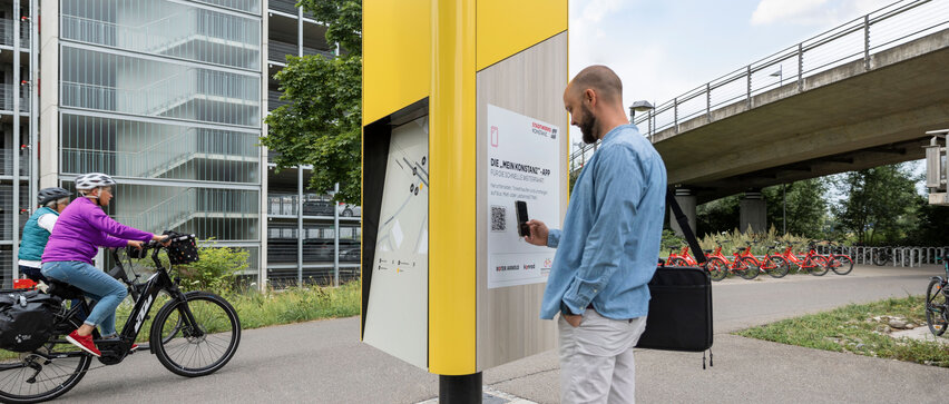 Mann scannt QR-Code an einer gelben Mobilitätsstation am Bahnhof Fürstenberg.
