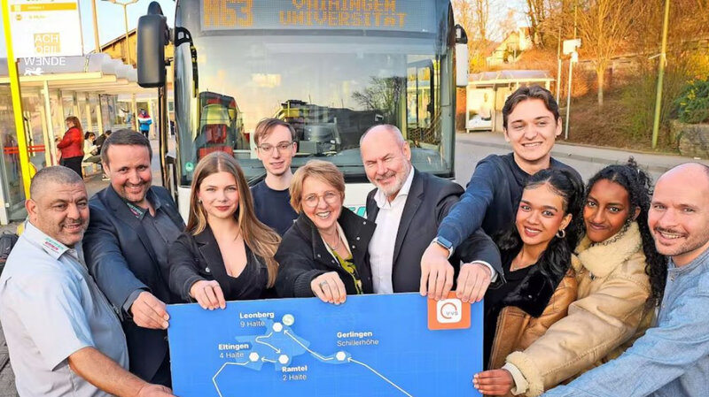 Eine Gruppe Menschen vor einem Bus die sich an einem großen Plakat festhalten.