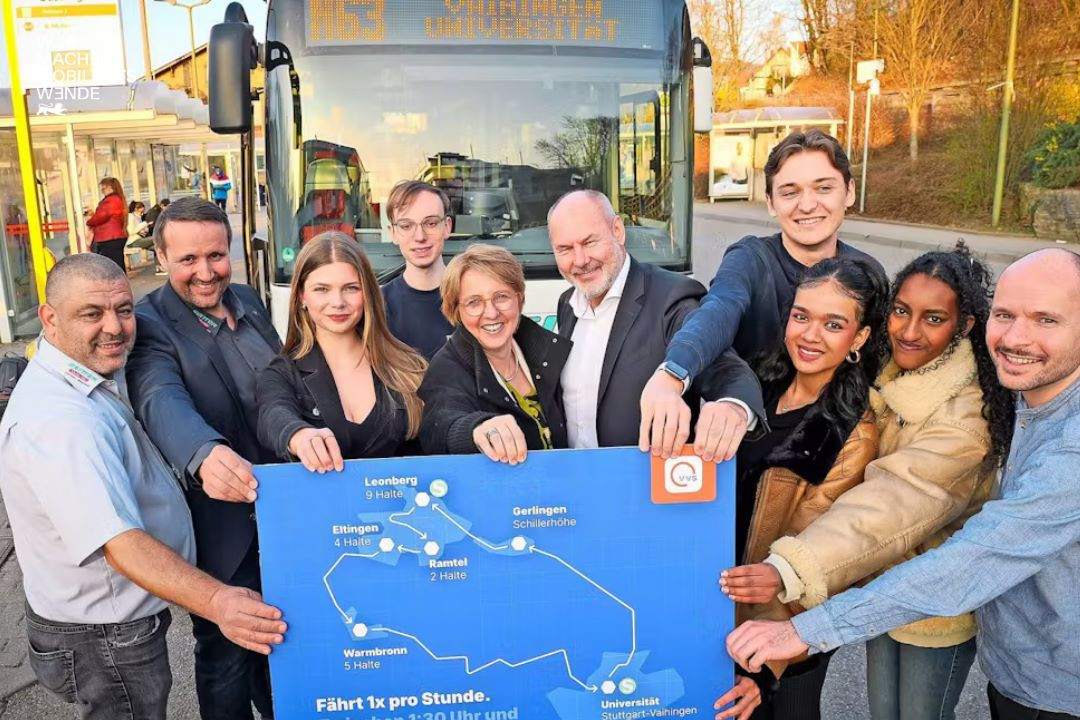 Eine Gruppe Menschen vor einem Bus die sich an einem großen Plakat festhalten.