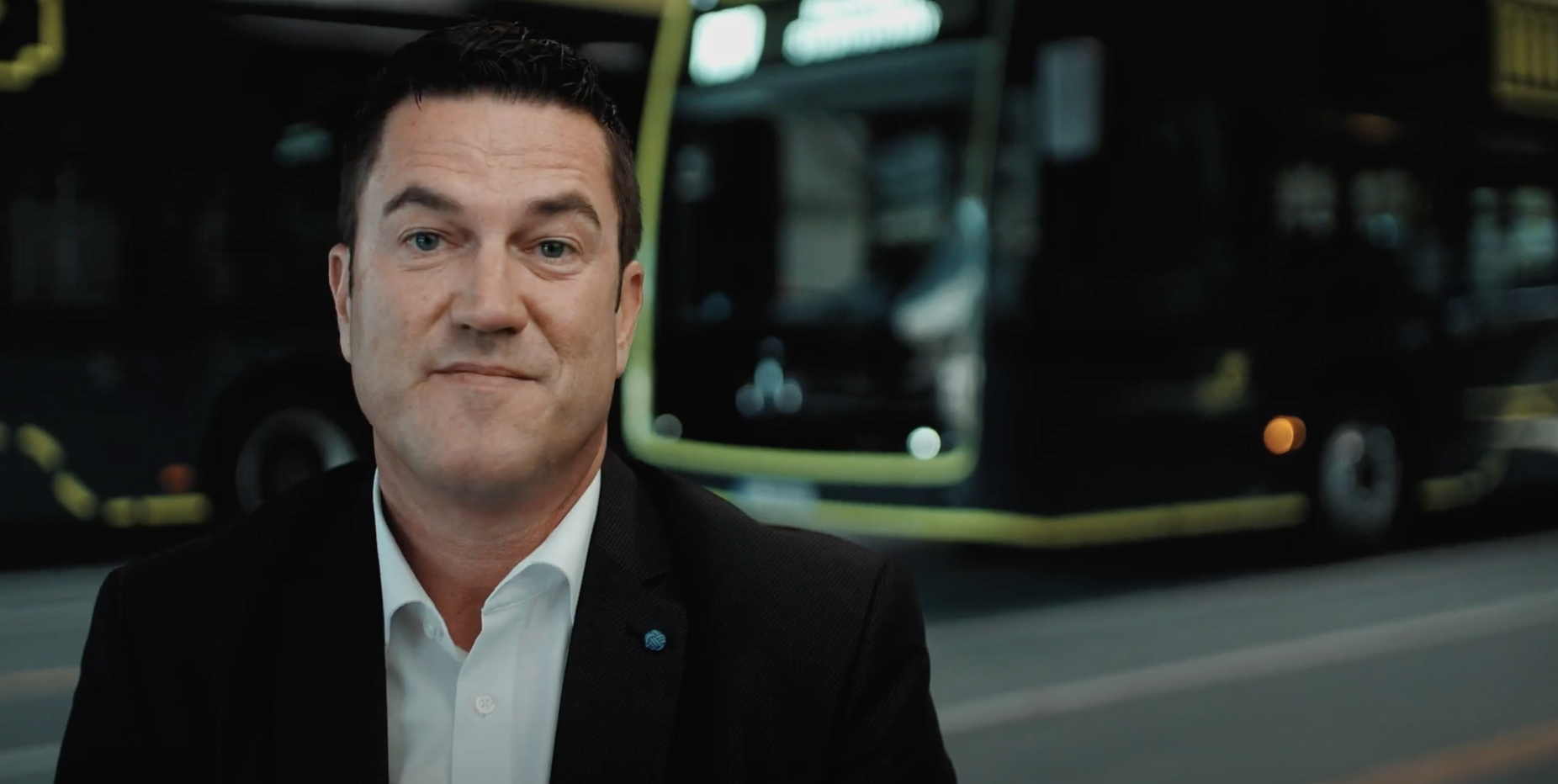 Ein Mann im Anzug der vor einem Bus steht.