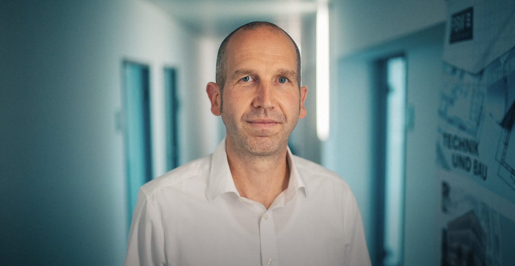 Mann im weißen Hemd steht in einem Flur.