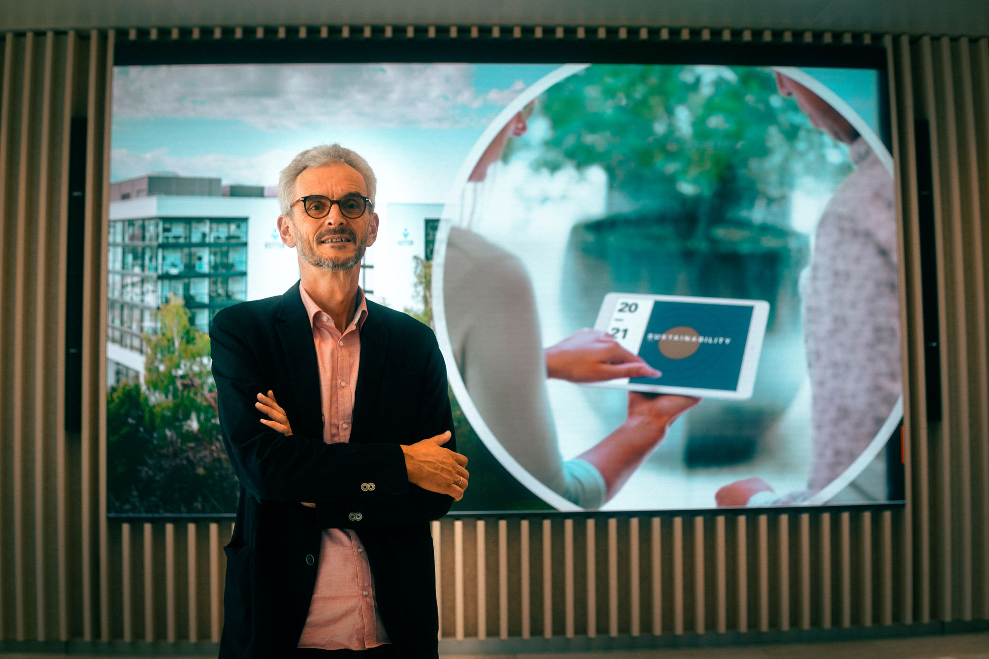 Ein Mann steht mit verschränkten Armen vor einem großen Bildschirm in einem Raum.