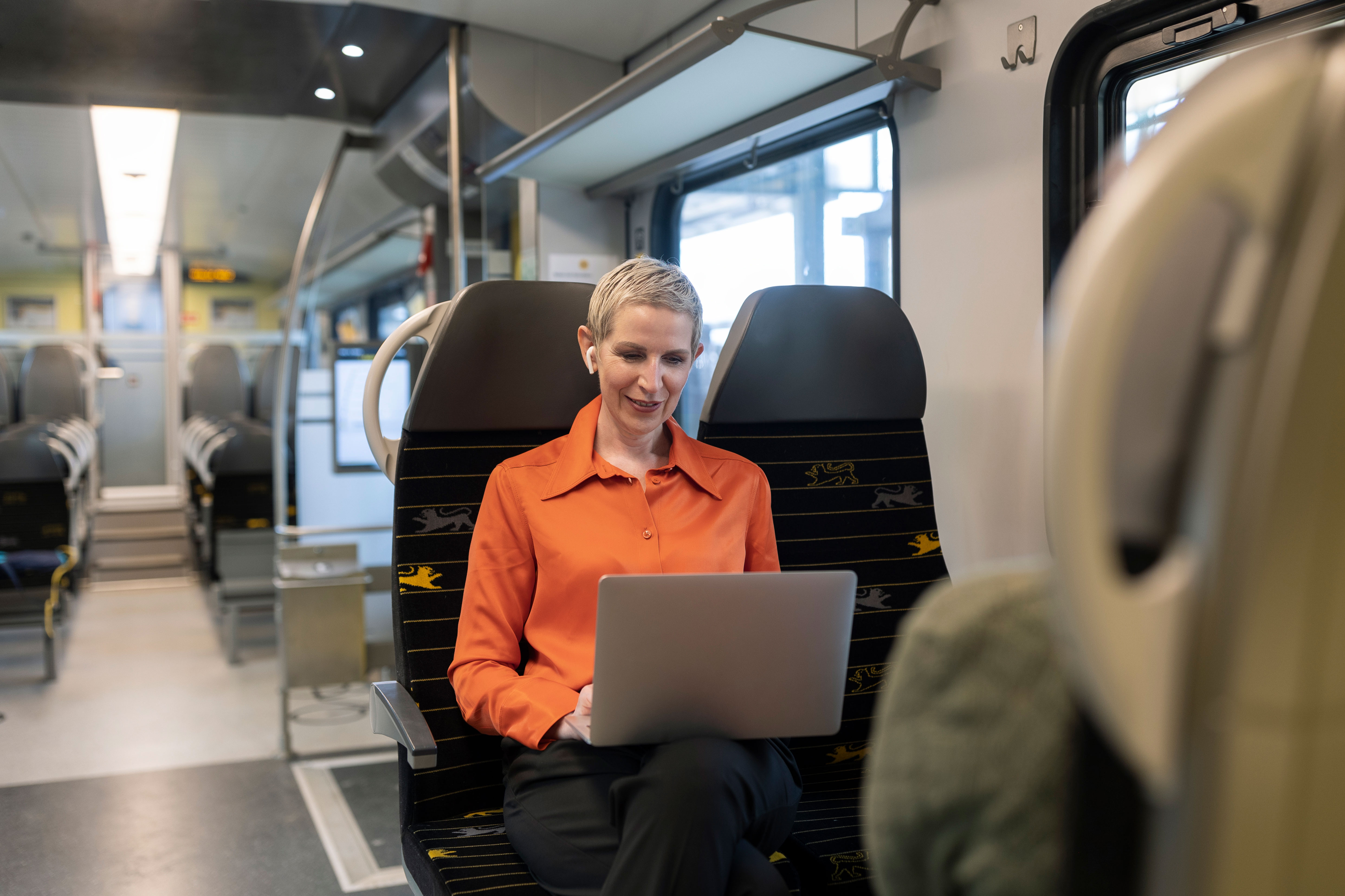 Frau arbeitet lächelnd mit Laptop im Zug, nutzt die Fahrtzeit effizient.