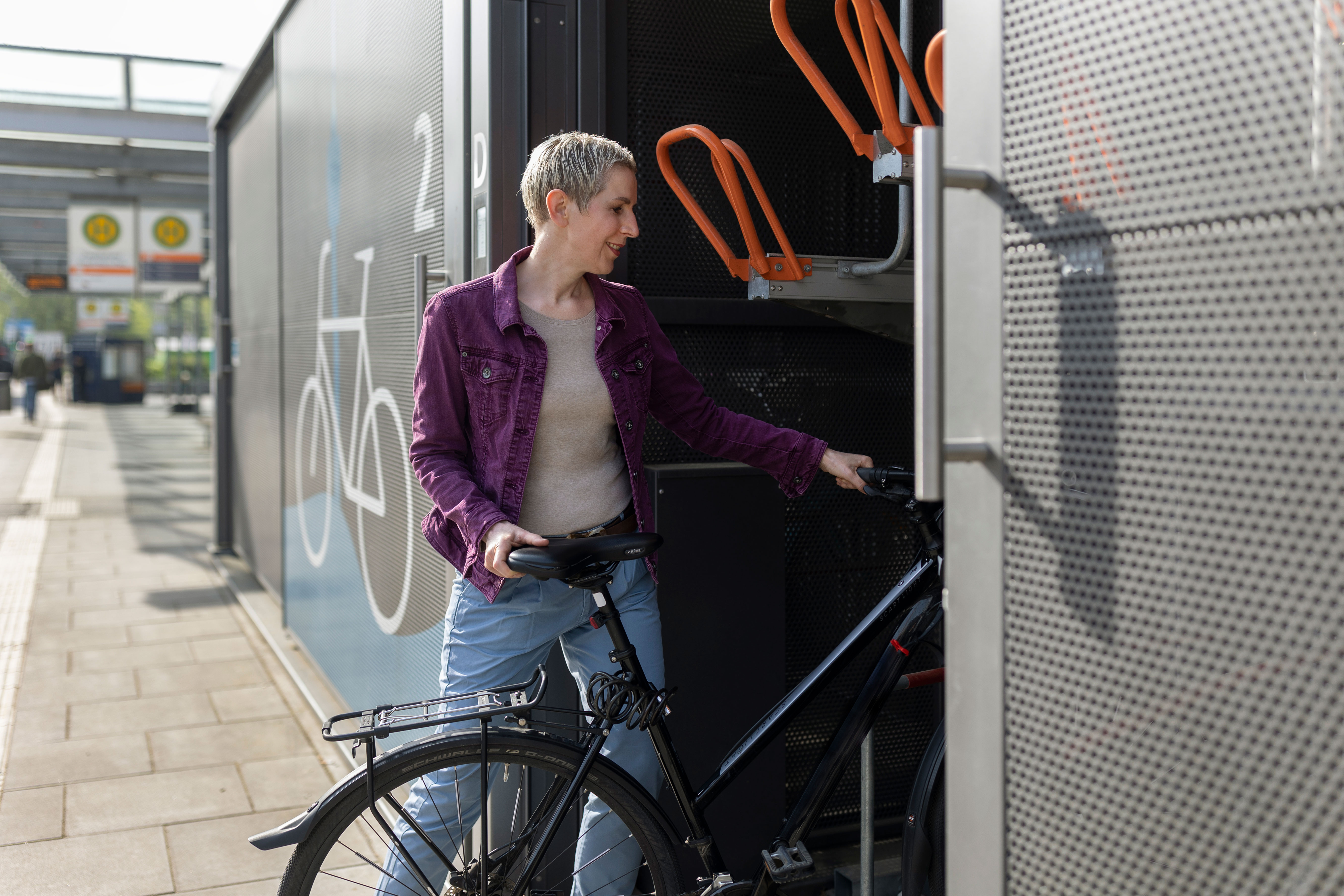 Frau stellt ihr Fahrrad in eine moderne Fahrradbox in einem Fahrradparkhaus.