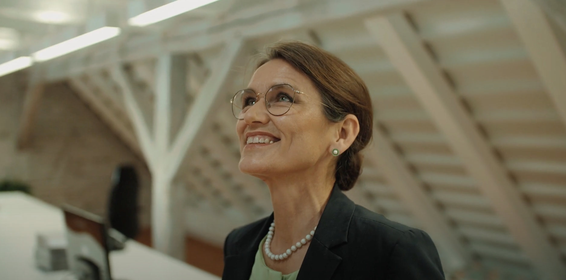 Eine Frau mit Brille und Zopf die lachend nach oben blickt.