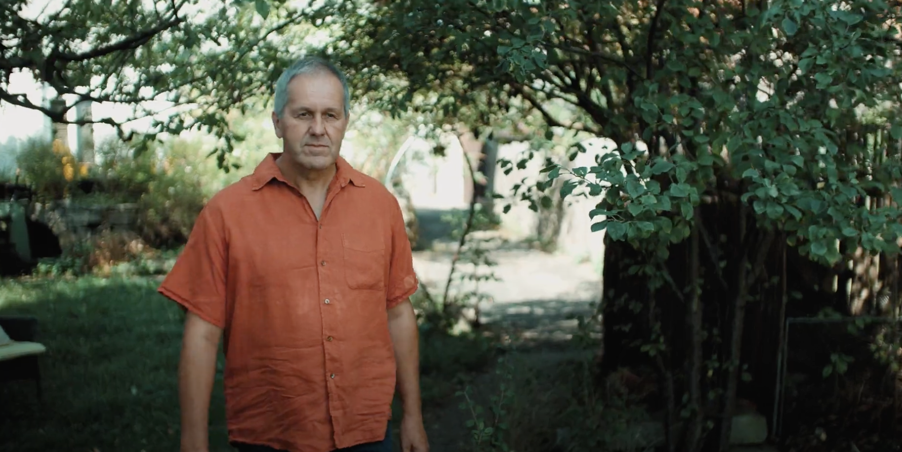 Ein Mann im roten Hemd der unter einem Baum steht.