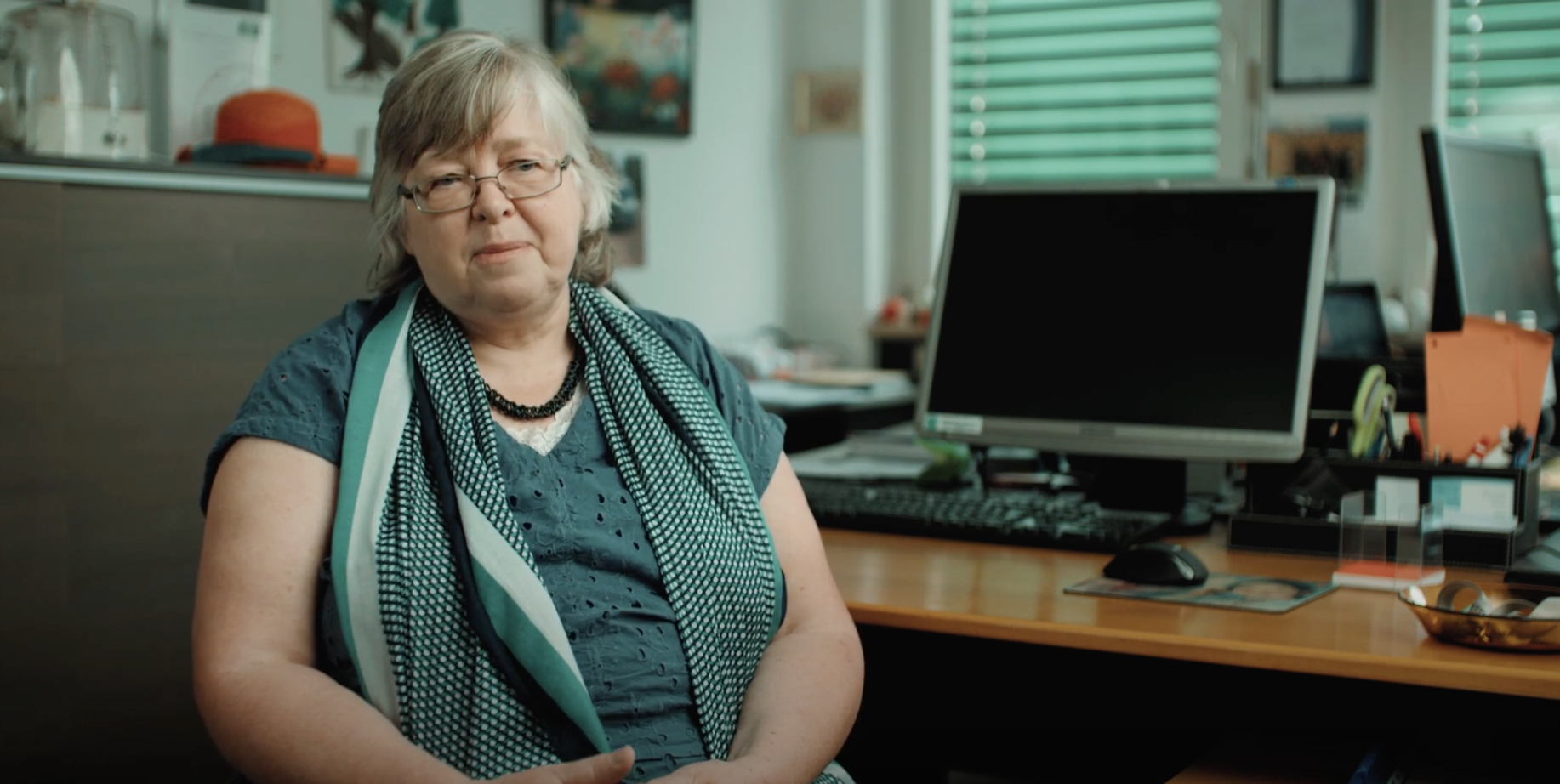 Eine Frau mit Brille die in einem Büroraum mit Computerbildschirm sitzt