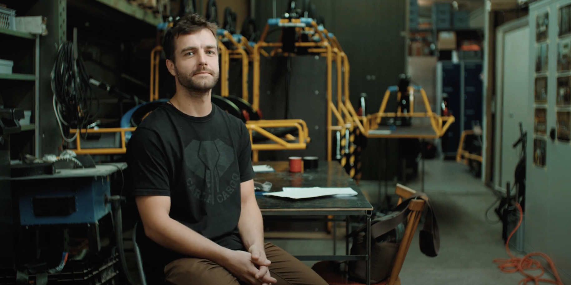 Ein junger Mann der in einer kleinen Lagerhalle sitzt.