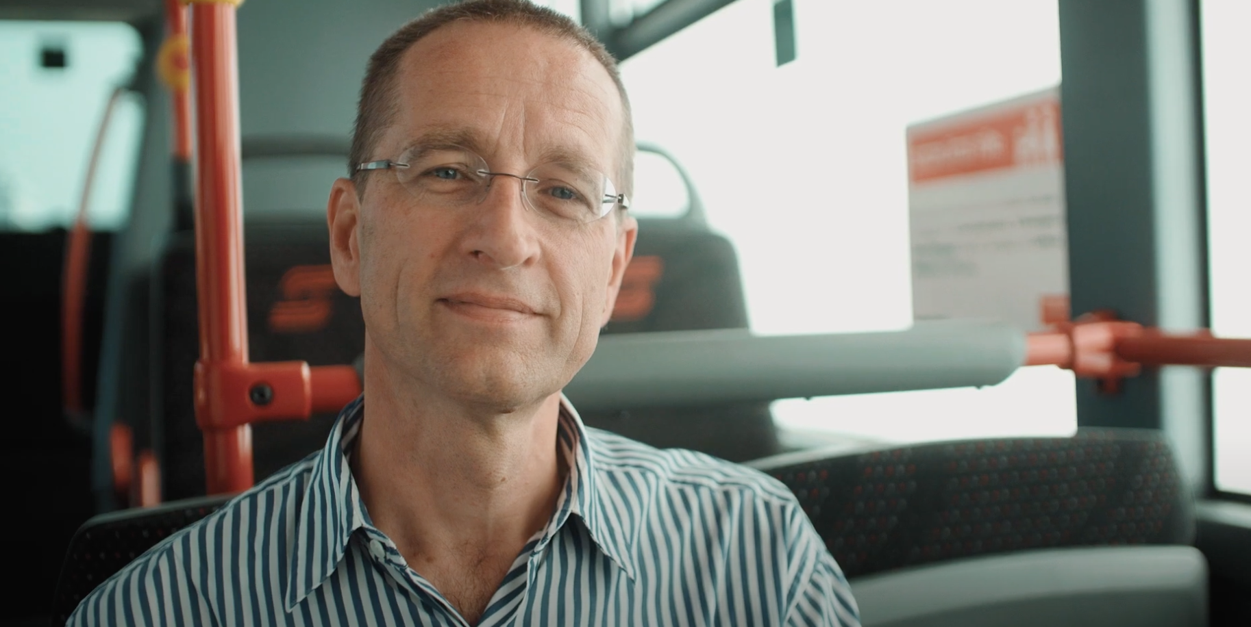 Ein Mann mit Brille der in einem Bus sitzt.