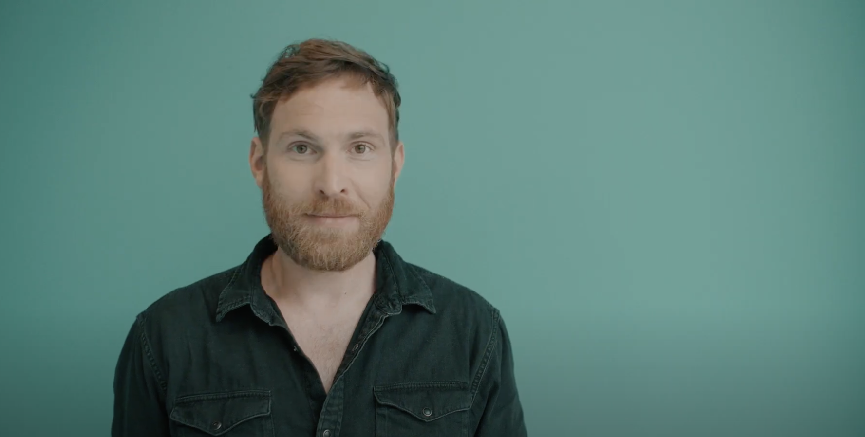 Mann mit Bart steht einer grünen Wand.