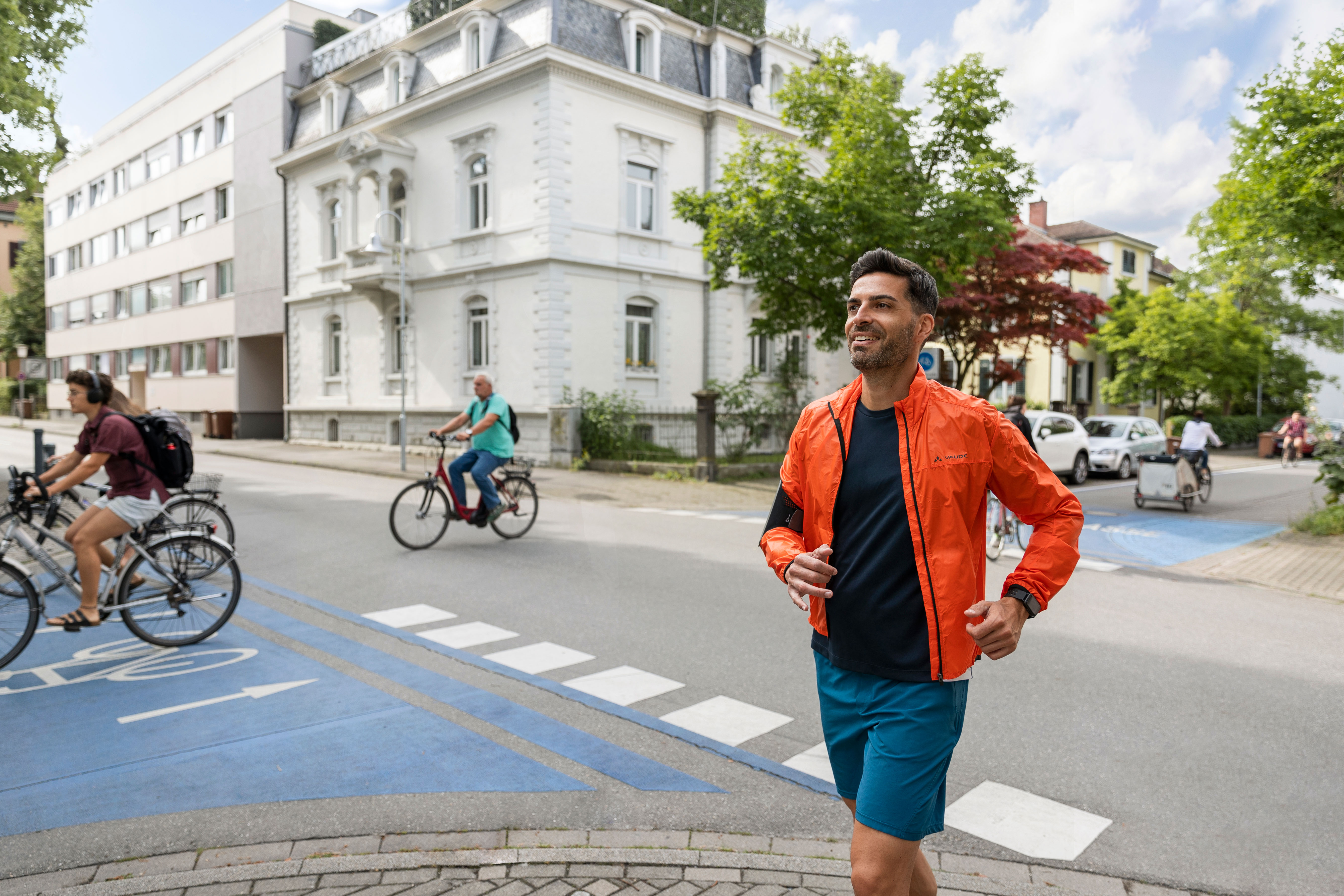 Mann joggt auf einer Straße mit blauem Radweg, im Hintergrund radeln Menschen.