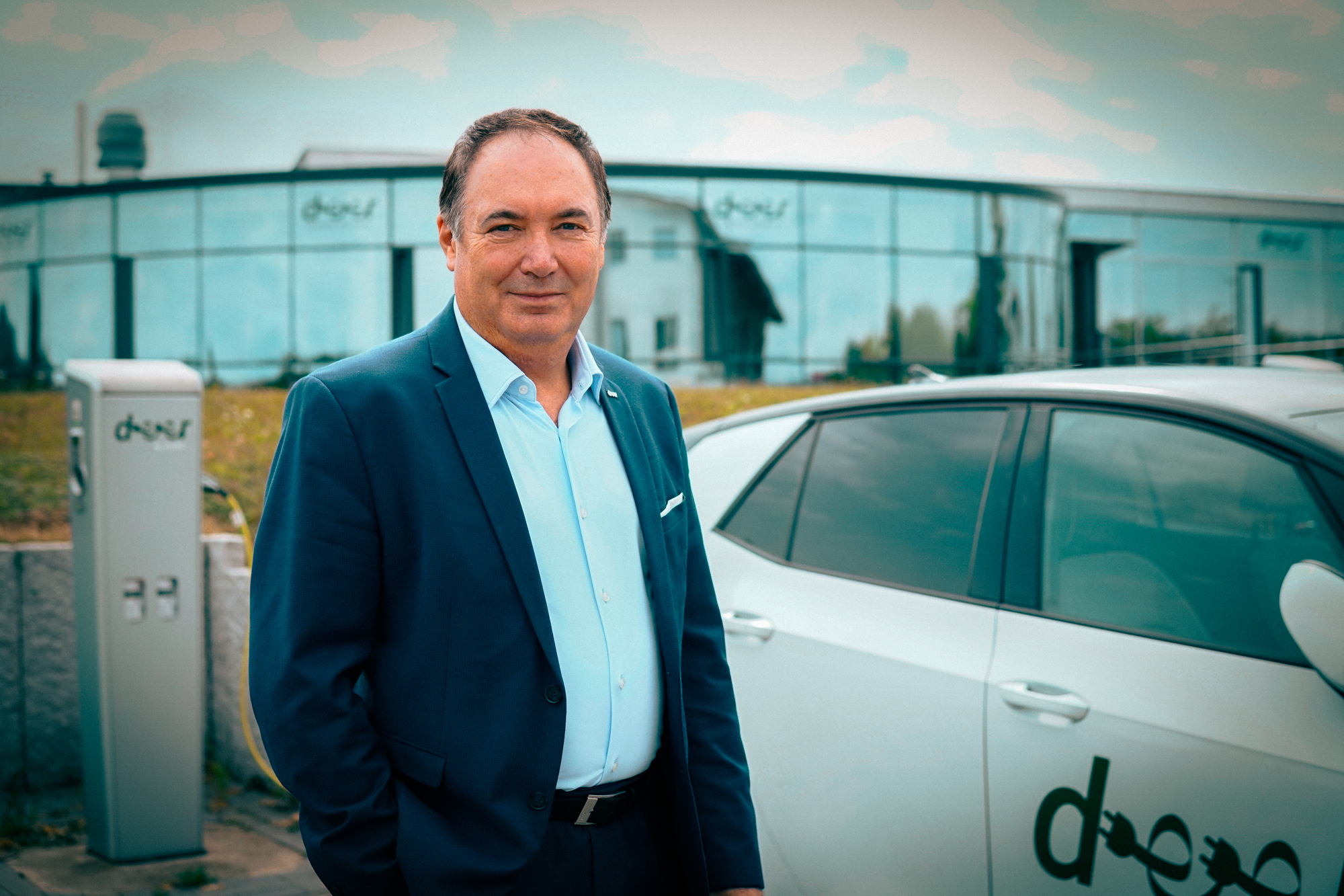 Ein Mann im Anzug steht vor einem Fahrzeug welches an einer E-Ladesäule geladen wird.