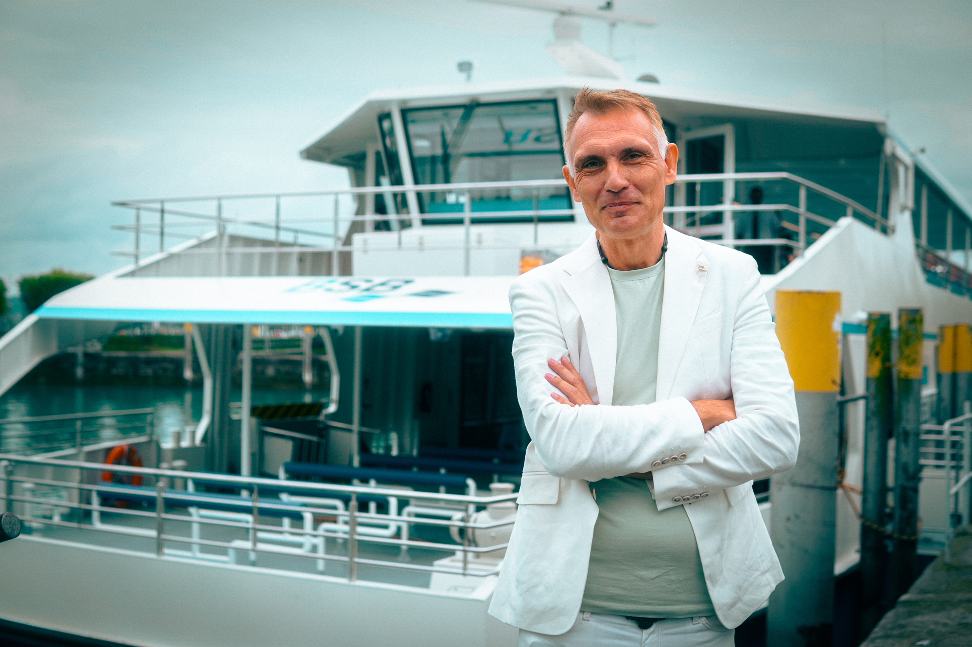 Ein Mann in weißem Anzug vor einem Fährboot.